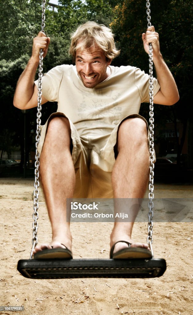 Uomo sorridente che giocano e su altalena al parco giochi - Foto stock royalty-free di Altalena