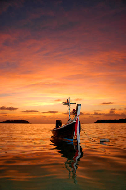 Scenic Sunset with Sun hid in clouds above sea horizon line, fishing boat drive to tropical jungle forest at left side of close up photo. Wavy evening sea, Thailand