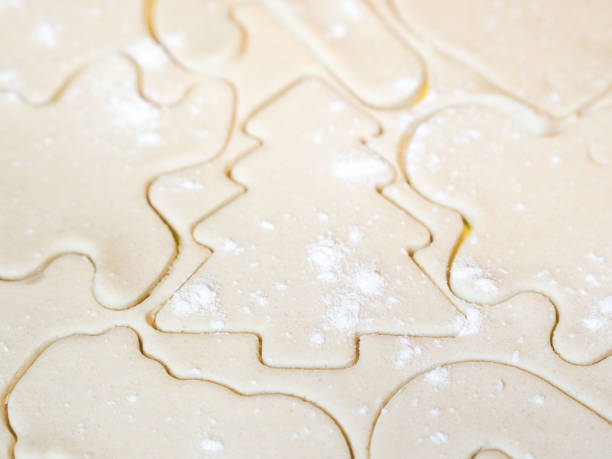 eine nahaufnahme von einem weihnachtsbaum-ausschnitt und anderen urlaub schablonen oder formen einschließlich lebkuchenmann schneiden in rohzucker cookie-teig mit mehl bestreut an der spitze einen schönen festlichen hintergrund. - candy cane christmas cookie raw food stock-fotos und bilder