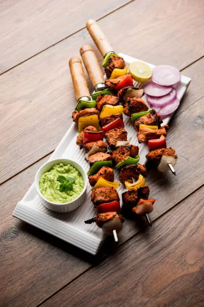 grilled chicken tikka on skewers.  served in a plate with green chutney and onion. Selective focus