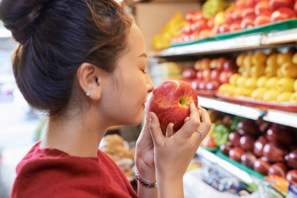 Woman smelling apple Young Vietnamese woman smelling ripe apple in supermarket smelling fruit apple food and drink stock pictures, royalty-free photos & images