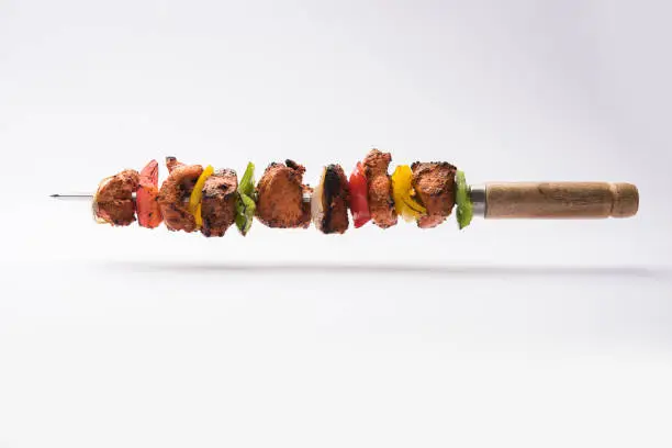 grilled chicken tikka on skewers.  served in a plate with green chutney and onion. Selective focus