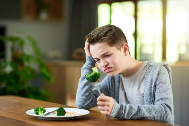 Cropped shot of a teenage boy refusing to eat his vegetables at home