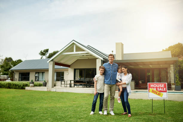 We're finally moving into a bigger house! Portrait of a family of four standing in front of their new home house for sale by owner stock pictures, royalty-free photos & images