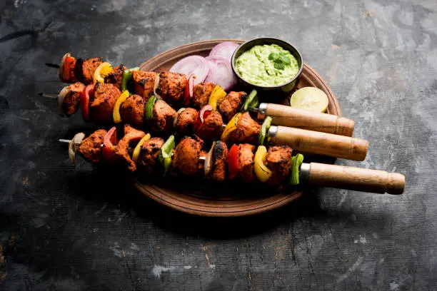 Spicy barbecued Chicken Tikka Boti on skewers served in a plate with green chutney - selective focus