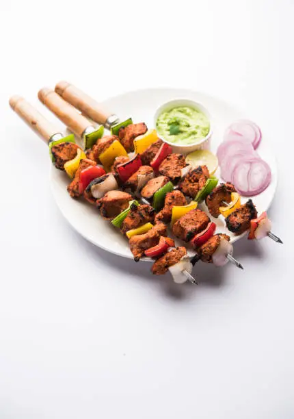 Spicy barbecued Chicken Tikka Boti on skewers served in a plate with green chutney - selective focus