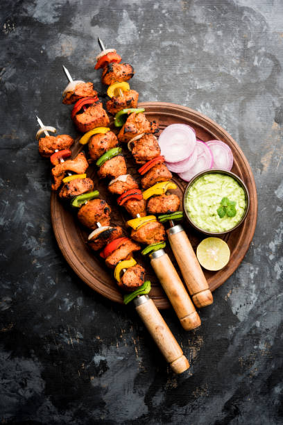 Spicy barbecued Chicken Tikka Boti on skewers served in a plate with green chutney - selective focus stock photo