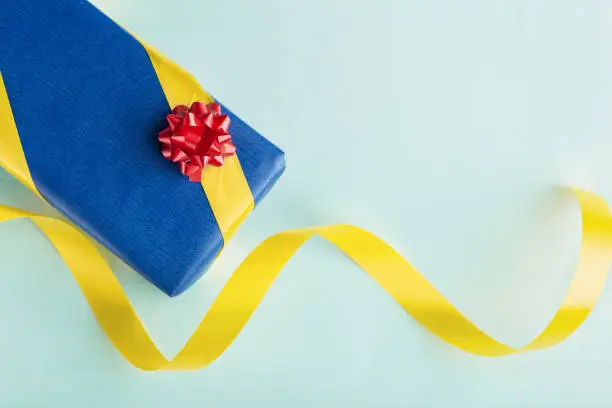 Blue gift box with yellow ribbon and red bow. Green-blue background. Top view. Copy space