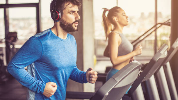 Treadmill exercise. Music and exercises go together. Couple working exercise on treadmill. Focus is on man. training equipment stock pictures, royalty-free photos & images