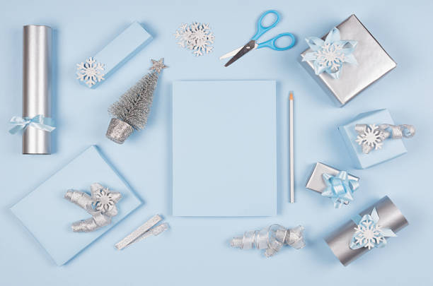 istock Christmas background for your design and text - blank paper and silver pencil, soft pastel blue and gift boxes with bows, christmas tree on blue backdrop, top view, copy space. 1081873512
