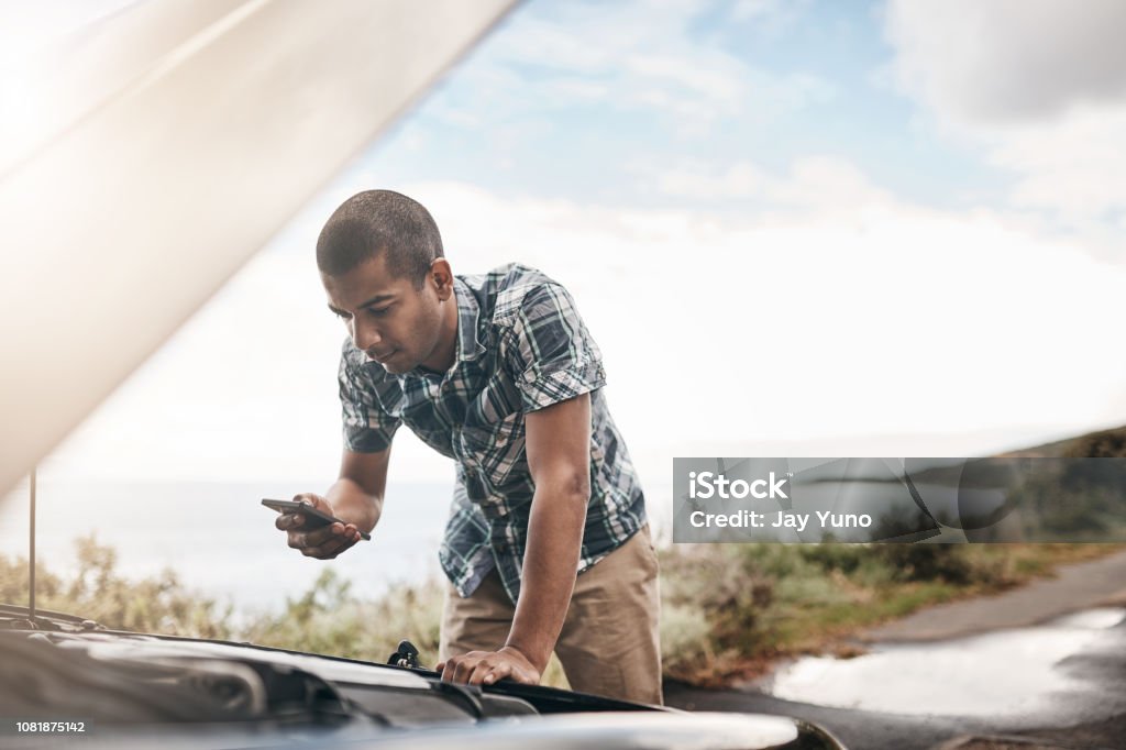 I'm stuck in the middle of nowhere, I need assistance Cropped shot of a young man with his broken down car on the side of a road Car Stock Photo