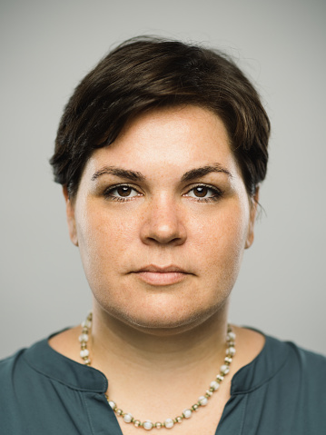 Close up portrait of caucasian mid adult woman with blank expression against gray background. Vertical shot of real woman staring in studio with long short brown hair and brown eyes. Photography from a DSLR camera. Sharp focus on eyes.