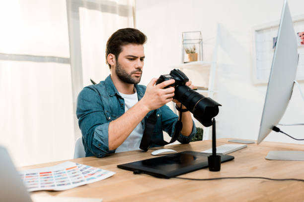 istock handsome professional young photographer using camera at workplace 1081881510