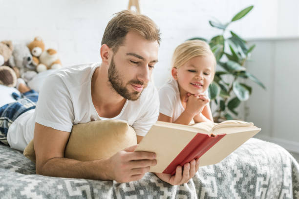 istock happy father and cute smiling daughter lying on bed and reading book 1081886676