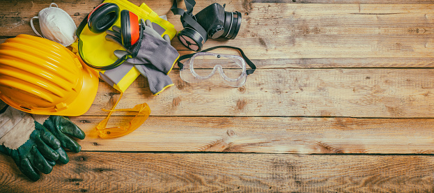 Construction safety. Protective hard hat, headphones, gloves and glasses on wooden background, banner, copy space, top view