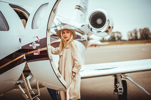 Joven rica rubia mujer mirando sobre su hombro al entrar en un avión privado estacionado en una pista de aeropuerto photo
