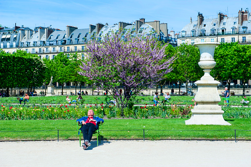 Paris, France - April 23, 2018: Man is resting on a bench and smoking cigar at Jardin des Tuileries, a public garden located between the Louvre Museum and the Place de la Concorde in Paris