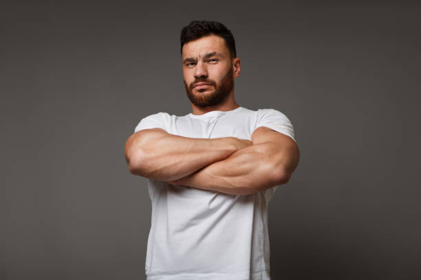 Suspicious young man with crossed big muscular arms Muscle concept - suspicious young man with crossed big muscular arms showing his arrogant strength and male power, looking down at camera muscular build stock pictures, royalty-free photos & images