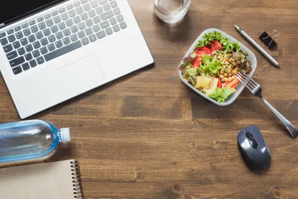 Healthy business lunch in office, salad, water on wooden table. Top view with copy space. Concept healthy nutrition. Lunchbox. Copy space.
