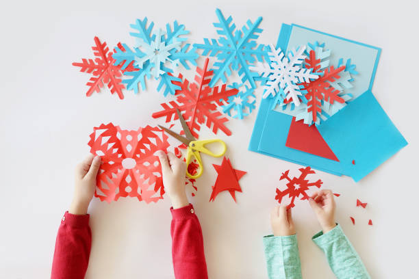 die hände von kindern auf einem weißen hintergrund blau und rot schneeflocken aus papier ausgeschnitten - snowflake winter blue paper stock-fotos und bilder
