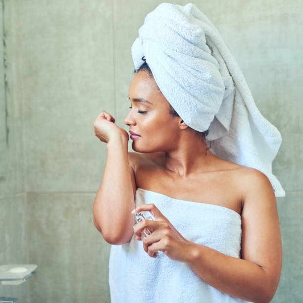 I love smelling good Cropped shot of a young woman spraying perfume after washing woman wrapped in bath towel stock pictures, royalty-free photos & images