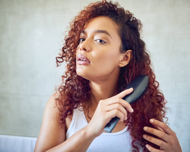 Brushing out those curls Cropped shot of a beautiful young woman brushing her hair in the bathroom at home brushing hair stock pictures, royalty-free photos & images