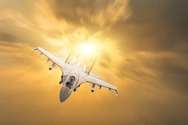 Furious military fighter jet with fire from engines flies in the orange sunset sky
