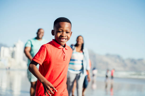 Waist up of boy running on beach and smiling Carefree energetic 7 year old boy looking at camera, smiling and cheerful, on holiday with parents in the background child running close up stock pictures, royalty-free photos & images