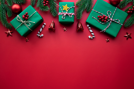 Christmas background concept. Top view of Christmas green and red gift box with spruce branches, pine cones, red berries and bell on white background.