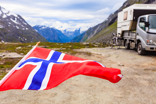 Norwegian flag waving on wind and camper car in mountains in the background. Travel, holidays and adventure concept.