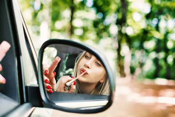 Young blonde woman applying a lip gloss in a passenger's seat in the car.