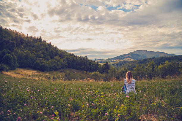 girl sitting on a green meadow and watching the countryside landscape. - rural watch imagens e fotografias de stock