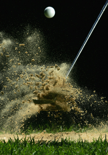 Male golfer shoting golf ball from sand bunker. Handsome asian golfer hitting golf ball with sand blast.