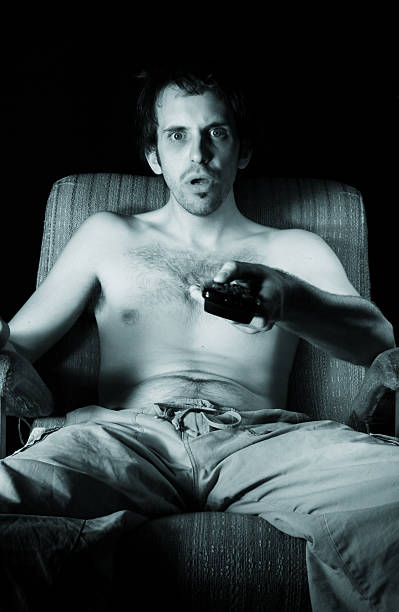 埋め込み式、上半身裸の男のラウンジ、テレビのリモコンを手に - shock color image vertical toned image ストックフォトと画像