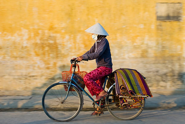 Woman Wearing Traditional Dress in Vietnam Riding Bicycle stock photo