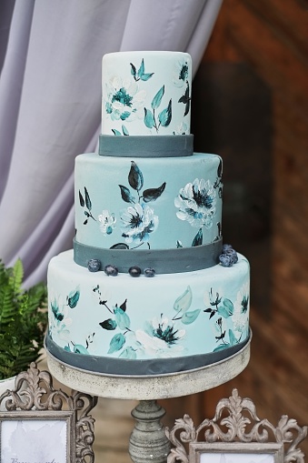 Beautiful blue three-tiered cake decorated with flowers on a stand, on the wedding table.
