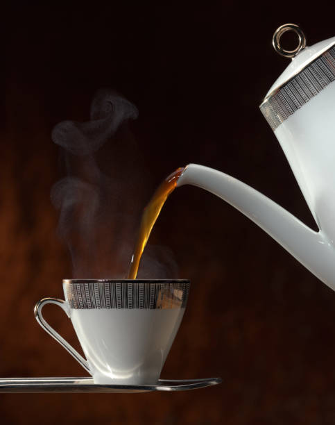 Teapot Pouring Hot Tea into Cup and Saucer stock photo