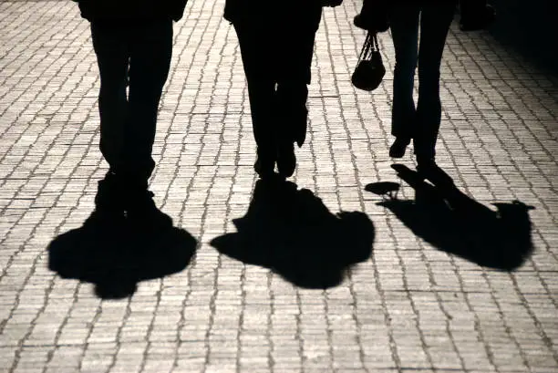 Photo of Silhouette of Three People Walking Down Cobblestone Road