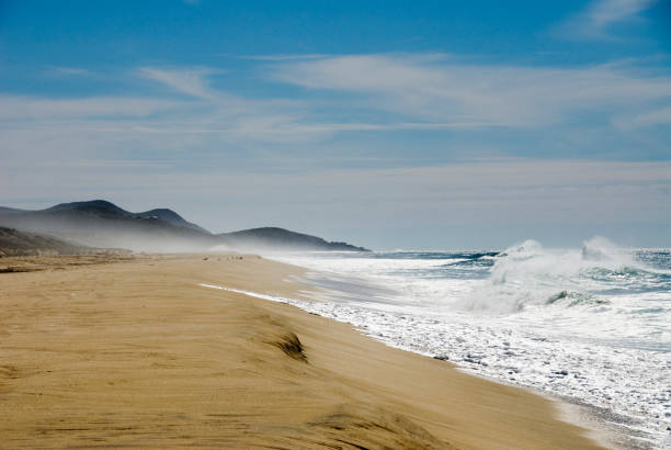 The ocean is calm and the beach is empty. The water is a beautiful shade of blue. The sand is dry and the beach is deserted