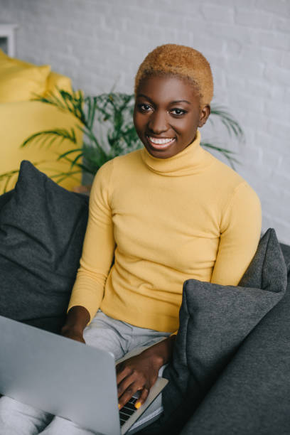 istock cheerful african american woman using laptop on sofa 1081956042