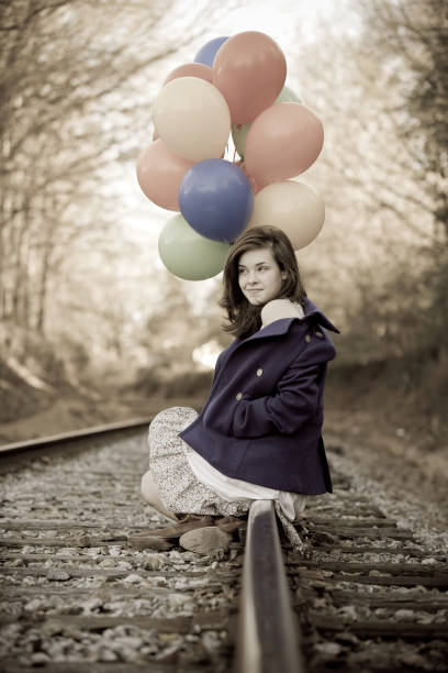 Jeune femme assise sur une voie ferrée en tenant des ballons - Photo