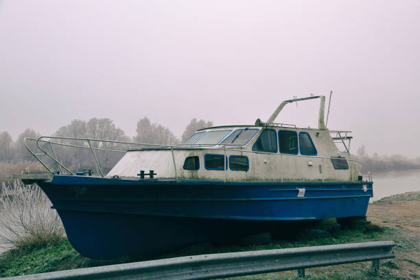 White-blue abandoned rusty boat on the banks of a misty river