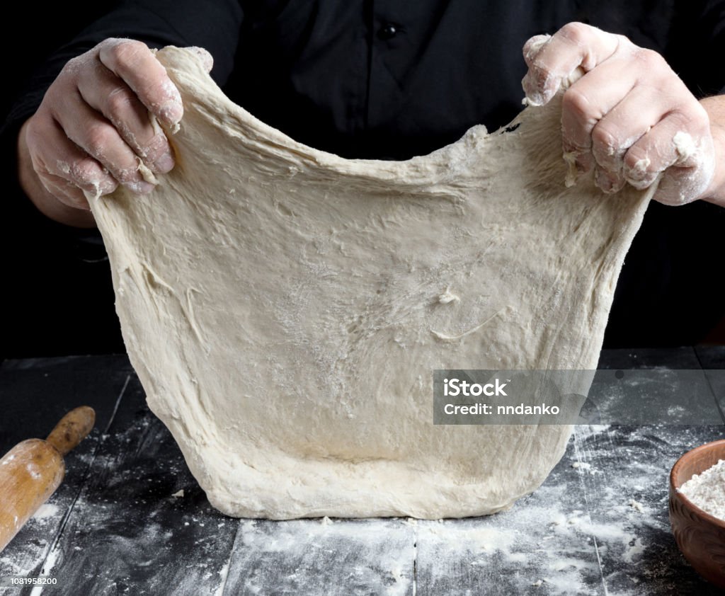 Chef in black jacket, kneads dough from white wheat flour Chef in black jacket, kneads dough from white wheat flour, close up 35-39 Years Stock Photo