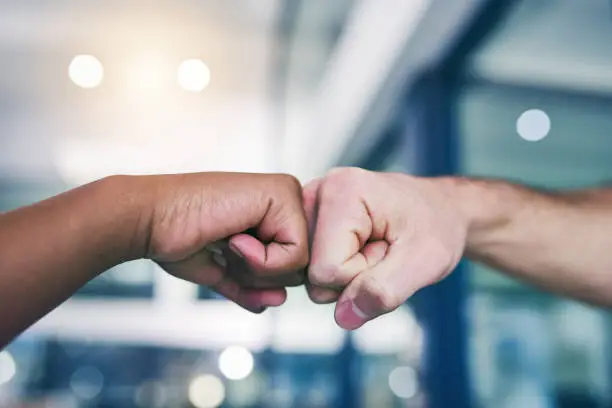Cropped shot of two people giving each other a fist bump in a modern office