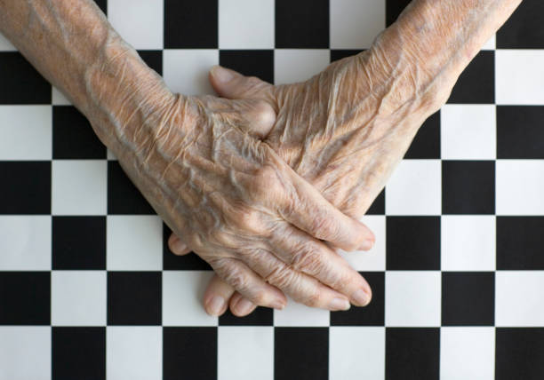 Senior Person's Hands Folded on Top of Checkerboard stock photo