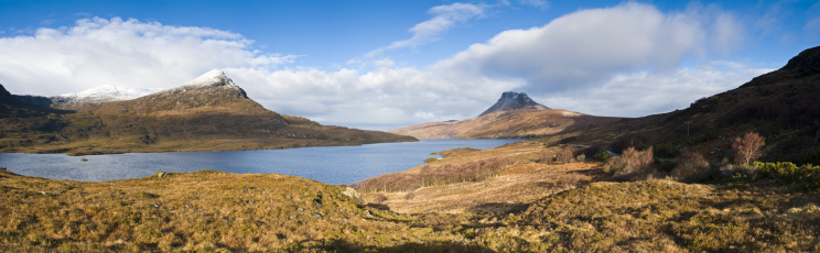 Sunlight and shadows on the golden grasslands, blue waters of Loch Lurgainn and snow capped peaks of Coigach and Stac Pollaidh in the remote highland wilds of the Inverpolly National Nature Reserve, Scotland, UK. Adobe RGB 1998 color profile.