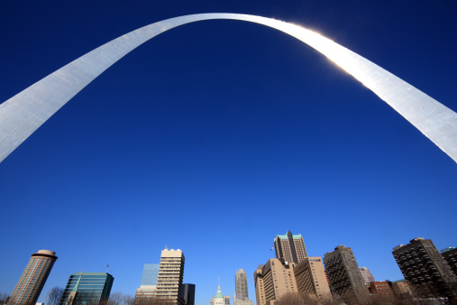 The arch is shining in the sunlight, and it is a striking contrast to the blue sky. The photo also captures the way the arch towers over the city of St. Louis.