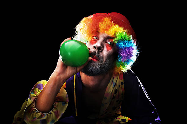 istock Creepy Looking Clown Blowing up Balloon on Black Background 108196946