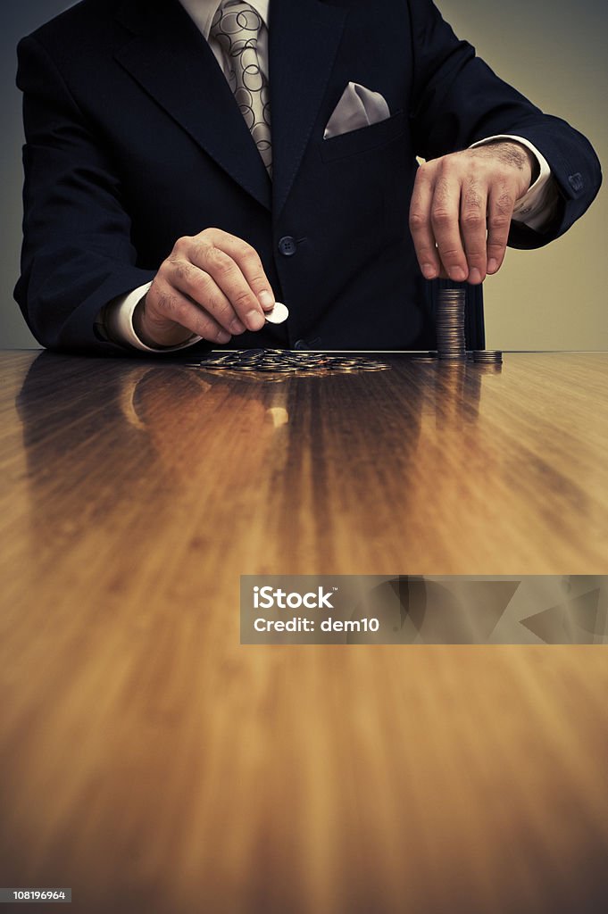 Empresário sentando na mesa e empilhamento de moedas - Foto de stock de Amor por Dinheiro royalty-free
