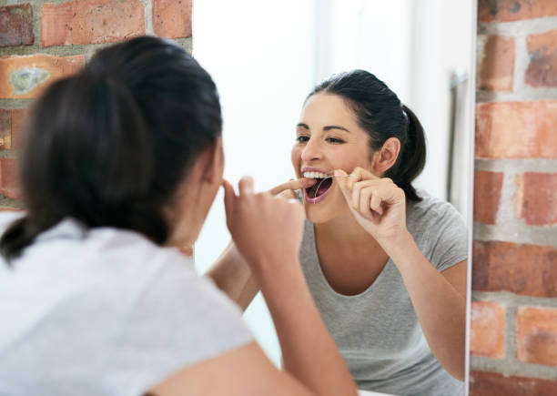 Making sure see reaches every spot Shot of a beautiful young woman flossing her teeth in the bathroom mirror dental floss stock pictures, royalty-free photos & images